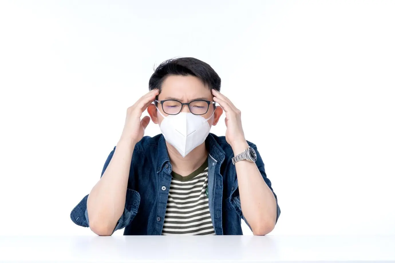 Nahaufnahme eines jungen asiatischen Geschäftsmanns, der eine Maske gegen Luftverschmutzung trägt; mit Gesten zeigt er Krankheit, Unwohlsein und schlechte Gesundheit infolge des Wetters und PM2,5-bedingter Umweltprobleme mit der Stadtluft.